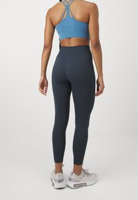 Světlemodrý sportovní crop top s křížovými ramínky, kombinovaný s vysokým pasem tmavě šedé legíny a světle šedými teniskami s růžovými akcenty.