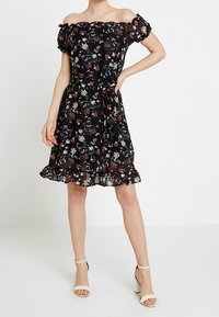 Svart blommig klänning med off-shoulder design, korta puffärmar, volangdetalj i fållen och ett livfullt mönster av flerspåriga blommor.