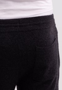 Donkergrijze, zachte fleece joggers met een elastische tailleband en een enkele achterzak; de textuur lijkt pluizig en warm.