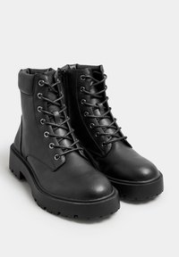 Botas de cuero negras hasta el tobillo con punta redondeada, parte delantera con cordones y cierre lateral de cremallera. Presentan una suela de goma gruesa y un cuello acolchado.