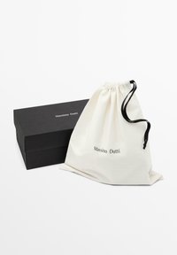Pochette blanche à cordon avec le logo "Massimo Dutti" à côté d'une boîte rectangulaire noire avec la même marque sur un fond blanc.