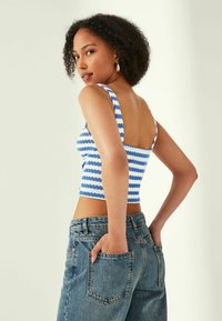 Modrý a bílý pruhovaný crop top s širokými ramínky a čtveratým zadním dílem, vyrobený z texturované látky, doplněný o světle modré džíny s vysokým pasem.
