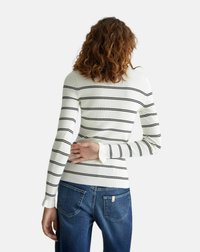 Maglietta a maniche lunghe a coste di colore bianco con sottili righe nere, caratterizzata da una silhouette aderente e polsini a contrasto, abbinata a jeans blu.