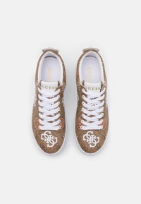 Bruine sneakers met een patroon, voorzien van witte veters en logo-accenten. Bovenwerk van stof met bloem- en logo-details; rubberen zool voor grip.