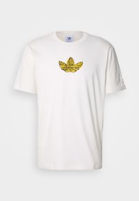 Vit bomulls-t-shirt med en gultryckt Adidas trefoil-logga på bröstet. Klassisk rund halsringning och korta ärmar. Mjuk textur.