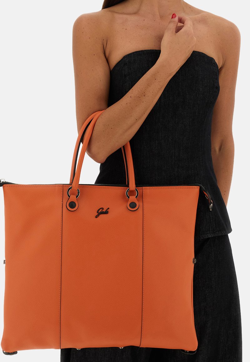 Borsa tote in pelle arancione con due manici, caratterizzata da una superficie testurizzata, dettagli in metallo nero e chiusura con zip. Dettaglio logo sulla parte anteriore.