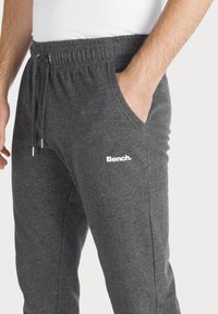 Gray jogger pants made of soft fabric, featuring an elastic waistband with a drawstring, side pockets, and a white "Bench." logo.