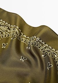 Sciarpa verde oliva in tessuto liscio con motivi paisley bianchi e floreali lungo i bordi. La superficie strutturata aumenta l'interesse visivo.