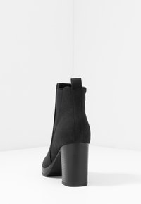 Botas negras hasta el tobillo con un acabado de ante texturizado, un tacón grueso y paneles laterales elásticos. Cuenta con una pestaña en la parte posterior para facilitar su uso.