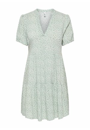 Vihreä lyhyt mekko, jossa valkoinen lehtikuvio, V-aukko, lyhyet pussihihat ja kerroksittainen hame.