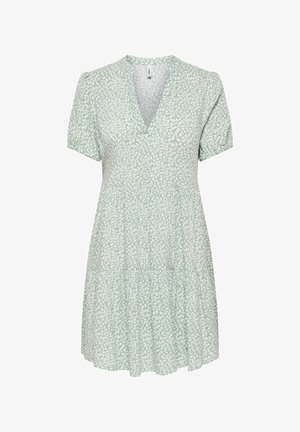 Vihreä lyhyt mekko, jossa valkoinen lehtikuvio, V-aukko, lyhyet pussihihat ja kerroksittainen hame.