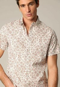 Chemise à manches courtes en tissu léger ; présente une base blanche avec des motifs floraux en rouge, turquoise et marron. Col classique.