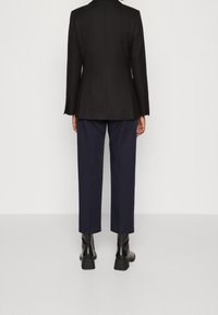 Svart skräddarsydd kavaj med en mjuk yta, som har en elegant design och långa ärmar, i kombination med marinblå cropped byxor och kraftiga svarta stövlar.