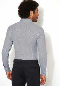 Overhemd met knoopsluiting van lichtgewicht stof, met een marineblauw en wit stippenpatroon, lange mouwen en een rechte kraag. Gepaarde met zwarte broeken.