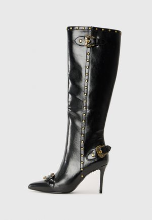 Black leather high-heeled boot with pointed toe, gold studs along the shaft, metallic buckle detail, and decorative accent at the heel.