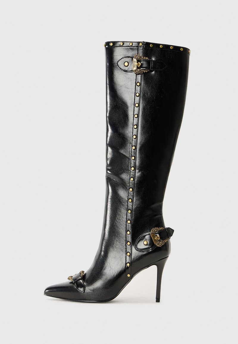 Juodas odinis aukštakulnis batu su smailiu pirštu, auksiniais kalnų akmenimis palei batus, metalinėmis sagtimis ir dekoratyviniu akcentu ant kulno.