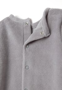 Sudadera de felpa gris con una textura suave, cuello redondeado y cierres de presión en el frente, con detalles de costura visibles.