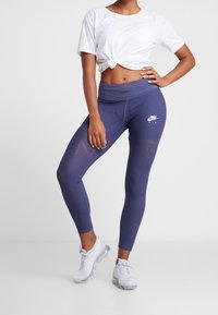 Marina högmidjade leggings med Nike-logotyp, med ett geometriskt mönster och stretchtyg. Kombinerat med en vit kortärmad knuten t-shirt.