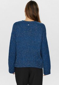 Zils adīts džemperis ar faktūru, apaļu kakla izgriezumu un ribotiem malām. Iekļautas nelielas pogas detaļas aizmugurē. Brīva piegriezuma.