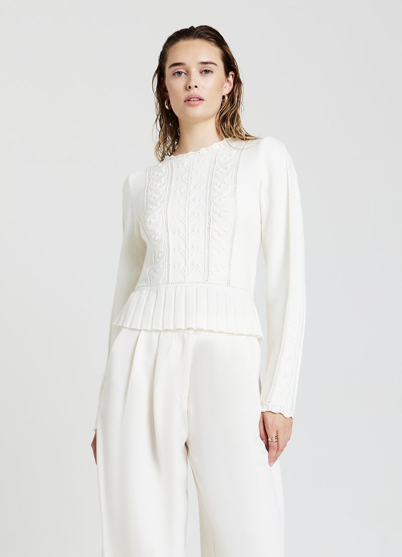 Weißer, gestrickter Pullover mit strukturierten Mustern und einem gerippten Peplum-Saum, kombiniert mit fließenden weißen Hosen. Lange Ärmel, runder Ausschnitt.