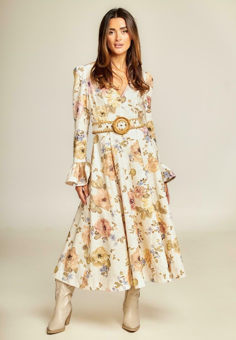Vestido midi floral en tela beige claro con mangas abullonadas hasta el codo, una falda con volantes y un cinturón trenzado con una hebilla decorativa.