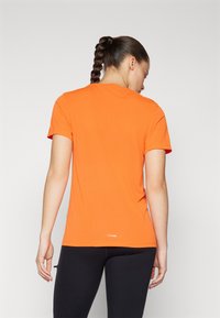 Oranžna kratka športna majica s kratkimi rokavi in krožnim izrezom, izdelana iz gladkega in lahkega materiala; ima logo blizu roba.
