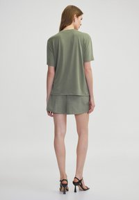 Camisa verde de manga corta con corte relajado, combinada con pantalones cortos verde claro. Textura suave, diseño minimalista y sutiles detalles de costura.