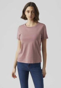 Lichtroze T-shirt met korte mouwen, een ronde hals en een relaxte pasvorm. Zacht katoen met een subtiele textuur. Gecombineerd met donkerblauwe jeans.