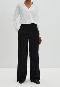 Blusa bianca a maniche lunghe con scollo a V abbinata a pantaloni a vita alta neri con gamba larga. Tessuto morbido, cuciture minime e vestibilità rilassata.