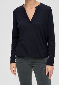 Mörkblå långärmad topp med V-ringning och mjukt material. Enkel design med avslappnad passform, tillsammans med mörkgrå åtsittande byxor.