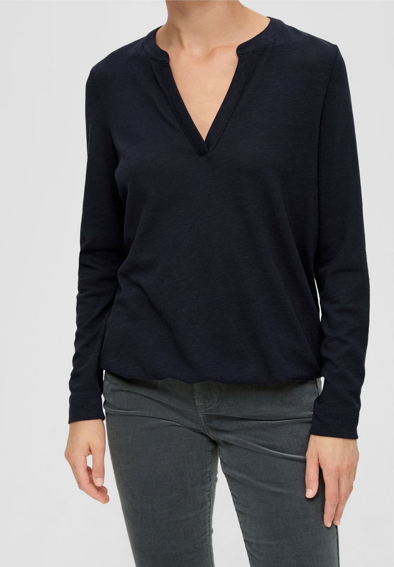 Mörkblå långärmad topp med V-ringning och mjukt material. Enkel design med avslappnad passform, tillsammans med mörkgrå åtsittande byxor.