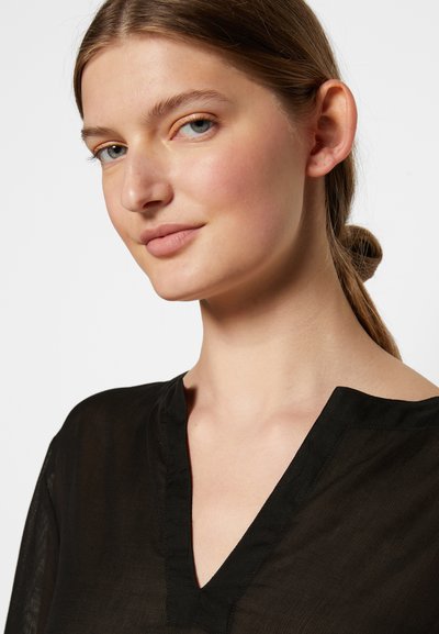 Blusa preta, leve, com um decote em V profundo e textura sutil. Apresenta um corte relaxado e um tecido macio que cai suavemente sobre os ombros.