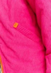 Jasnoróżowa bluza polarowa o żebrowanej fakturze. Posiada pomarańczową metkę, widoczny zamek błyskawiczny oraz miękkie wykończenie materiału.