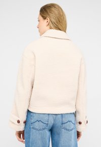 Jacke aus cremefarbenem Kunst-Lammfell mit breitem Kragen, knöpfbaren Manschetten und einem Schnitt oberhalb der Taille. Strukturierte, warme und lässige Gestaltung.