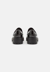 Scarpe in vernice nera con un design arrotondato, suola spessa, linguetta sul tallone e dettagli di cucitura discreti sulla tomaia.