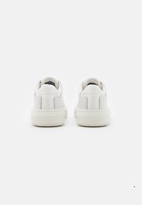 Ett par vita låga sneakers sedd från baksidan, med tjocka sulor och "Calvin Klein"-logotyp på hälarna.