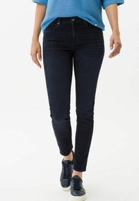Donkerblauwe skinny jeans met een gladde textuur, voorzien van een knoopsluiting aan de voorkant en zijzakken, gecombineerd met marineblauwe sneakers.