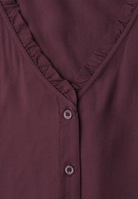 Gros plan sur un vêtement violet avec un décolleté en V, comportant une petite bordure froncée et deux boutons assortis à l'avant.