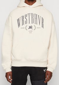 Felpa con cappuccio beige con una grande grafica frontale in testo grigio scuro e un logo di un cavallo alato. Presenta una tasca a canguro e polsini a coste.