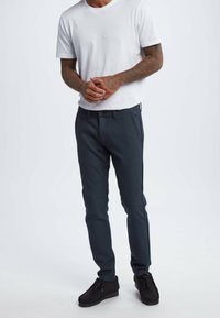 Mörkgrå byxor för män i strukturerad tyg, slim fit med framfickor, kombinerade med en vit T-shirt och svarta skor.