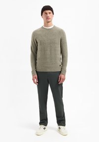 Grijze gebreide sweater met een ronde hals, gestructureerde stof en geribbelde manchetten, gecombineerd met donkergroene broek en witte sneakers, gedragen met een bruine beanie.