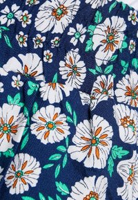 Granatowy materiał z białymi kwiatami o pomarańczowych środkach i zielonymi liśćmi, haftowany w szczegółowy wzór z marszczoną teksturą.