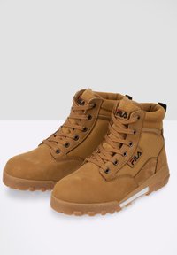 Bottines en suede marron avec col rembourré, lacets ronds, semelles en caoutchouc et accents du logo Fila. Caractéristiques d'une combinaison de matériaux lisses et texturés.