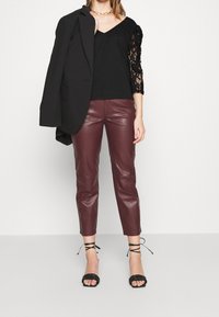 Musta V-pääntie toppi pitsihihnoilla, burgundin väriset tekonahkahousut ja mustat kapeat sandaalit. Mukana musta bleiseri heitettynä olalle.