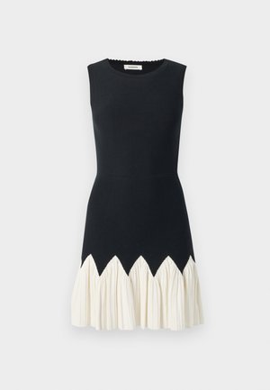 Ärmlös klänning med en åtsittande svart bodice, krämfärgad volang nertill med ett zigzag-mönster. Slät textur, rund halsringning, längd till mitten av låret.