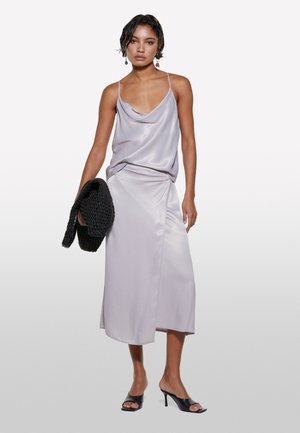 Ensemble comprenant un haut et une jupe en satin dans un léger lavande ; tombé élégant, légère brillance ; associé à un sac à main en toile noir et des talons ouverts.