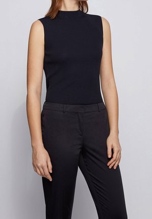 Czarny top bez rękawów wykonany z prążkowanej dzianiny, z wysokim kołnierzem, dopasowanym krojem i gładką fakturą, w połączeniu z ciemnymi spodniami.