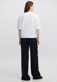 Witte top met korte mouwen en een ontspannen pasvorm, voorzien van een ronde hals en een gladde textuur, gecombineerd met zwarte, wijde broek.