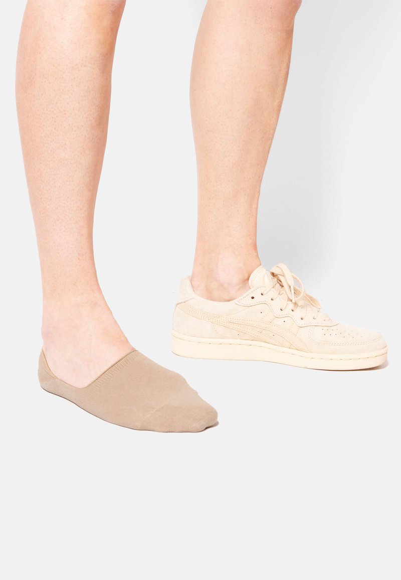 Beige No-Show Socken links, mit glatter Textur. Beige Wildledersneaker rechts, mit Schnürsenkeln und perforierten Details.