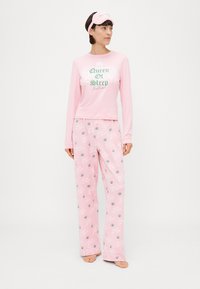 Conjunto de pijama rosa claro, com uma blusa de mangas longas com o texto "Rainha do Sono" e calças largas com um padrão de coroas. Inclui uma máscara de dormir combinando.